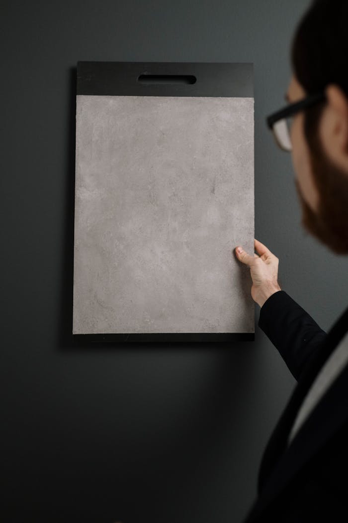 A man holds a textured sample board against a dark wall. Vertical shot.